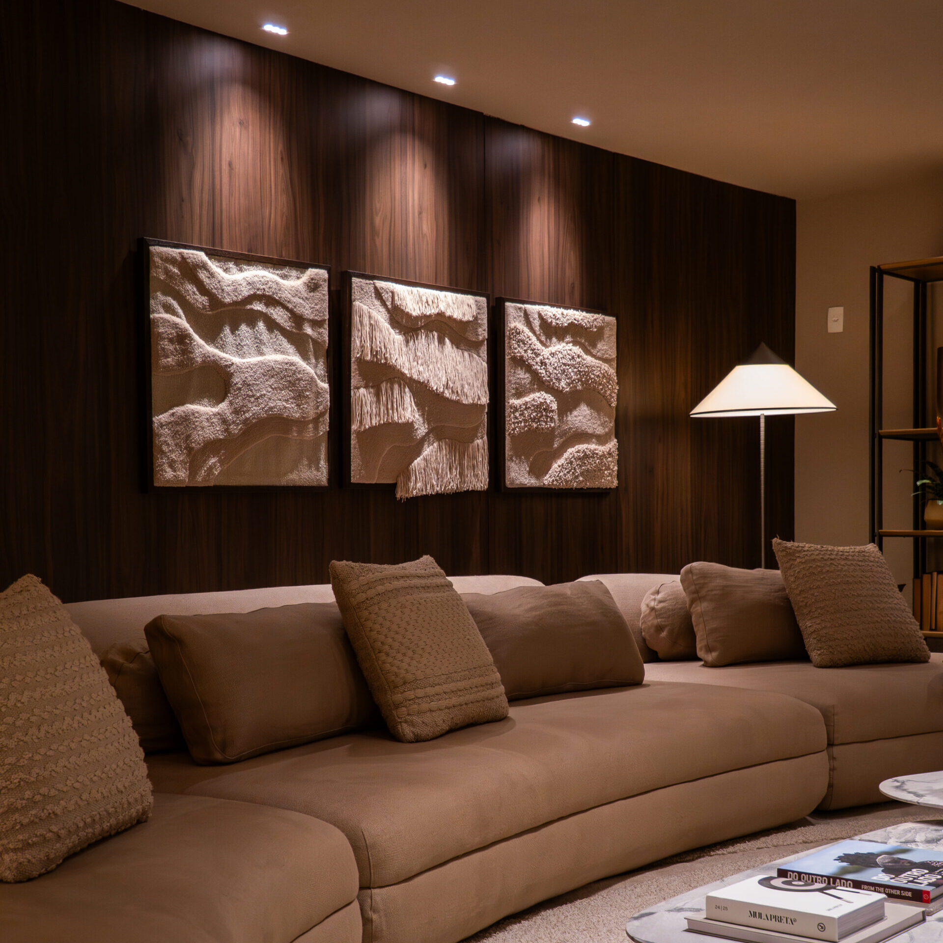 Iluminação estratégica valorizando painel de madeira e obras de arte