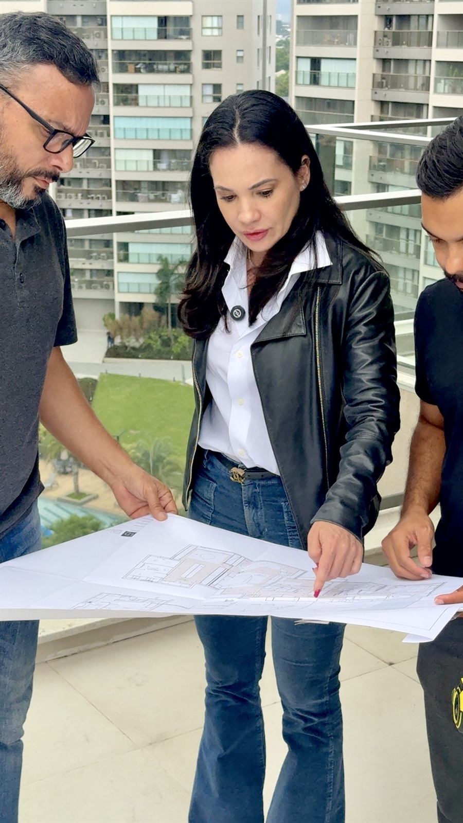 Arquiteta Leila Dionizios analisa a planta de um projeto de arquitetura com a equipe na varanda do imóvel